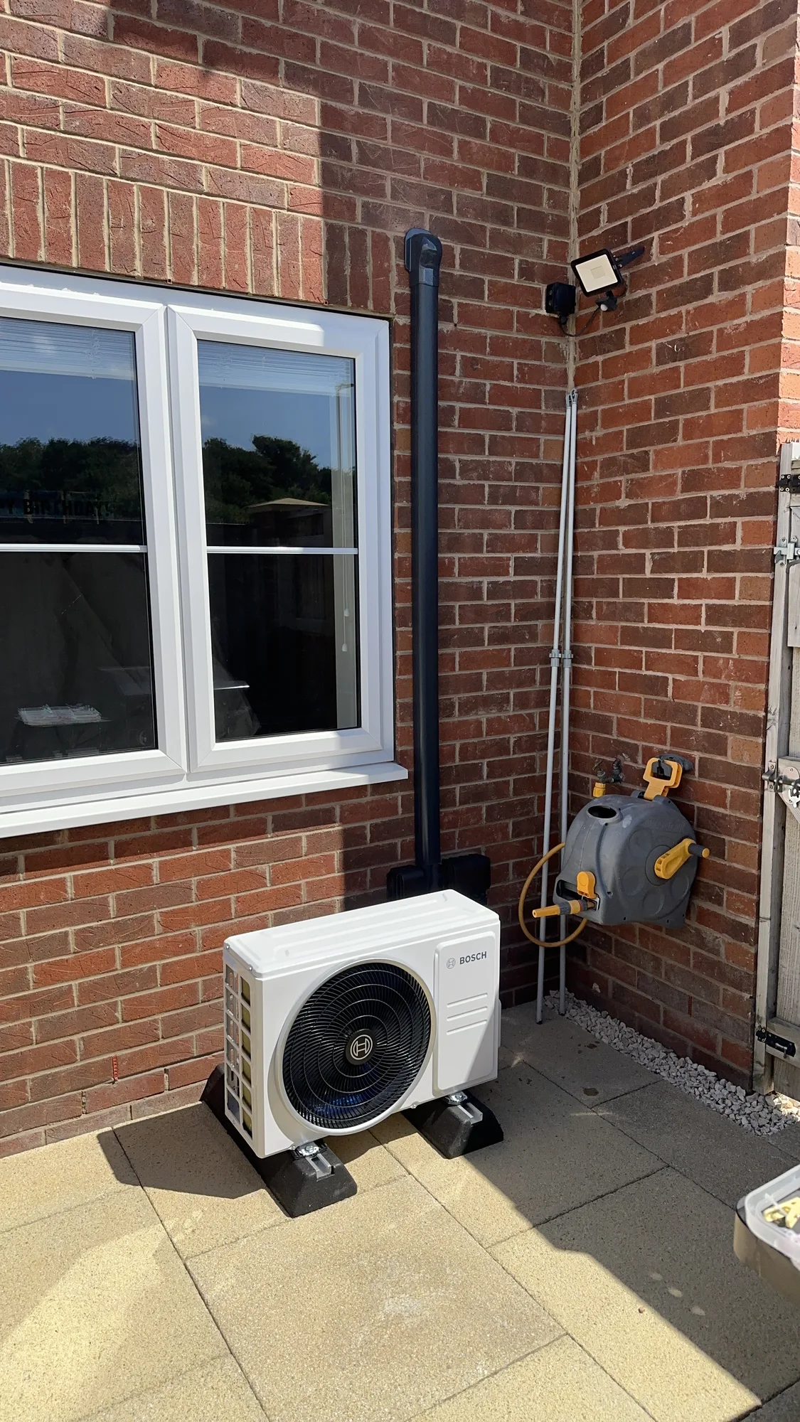 Air conditioning outdoor condenser on a brick patio beside a window