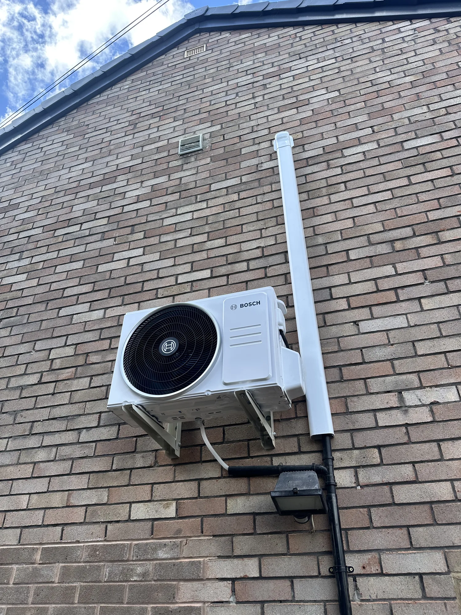 Air conditioning outdoor condenser mounted high on a brick wall