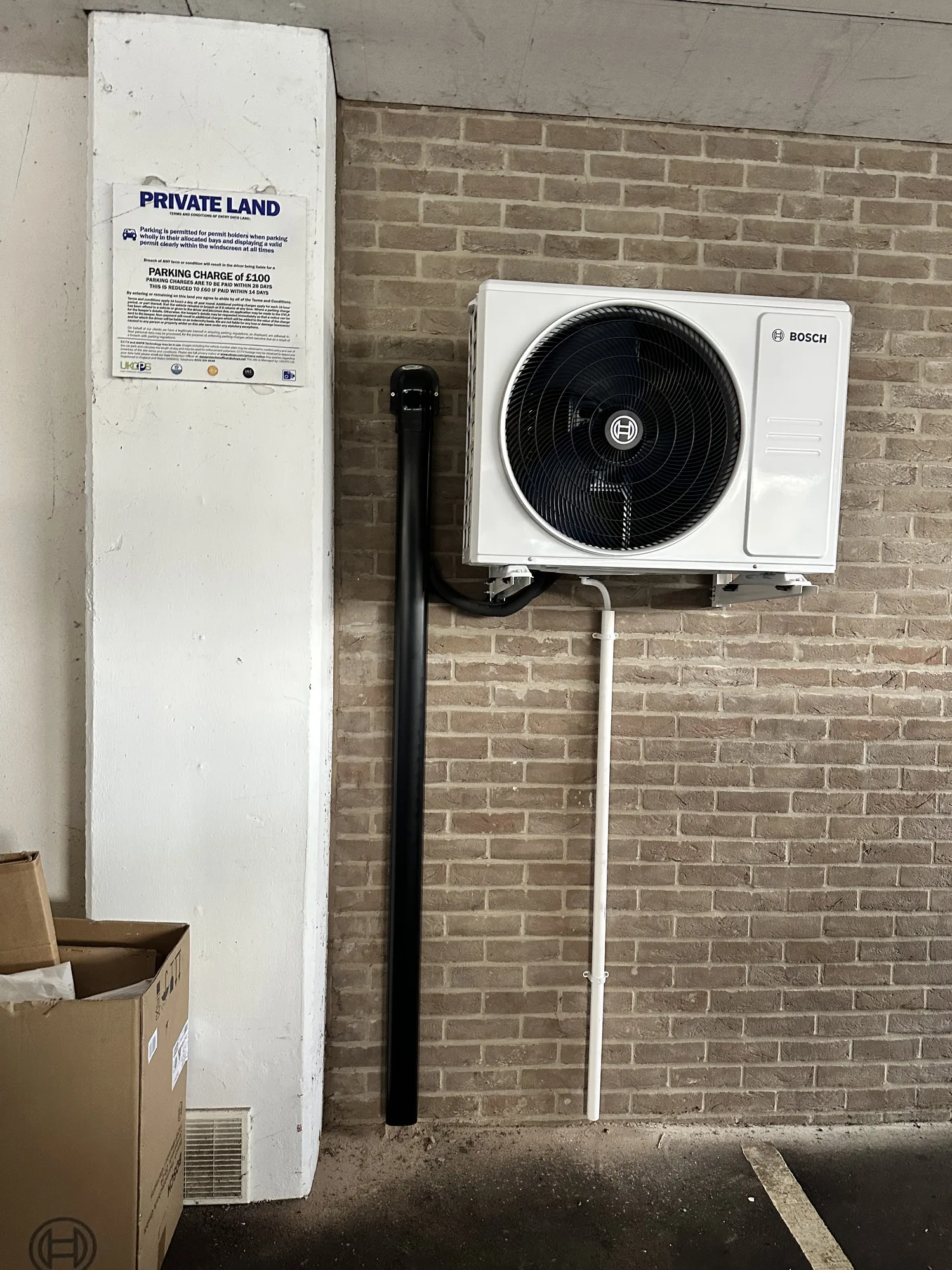 Air conditioning outdoor condenser installed on a brick garage wall