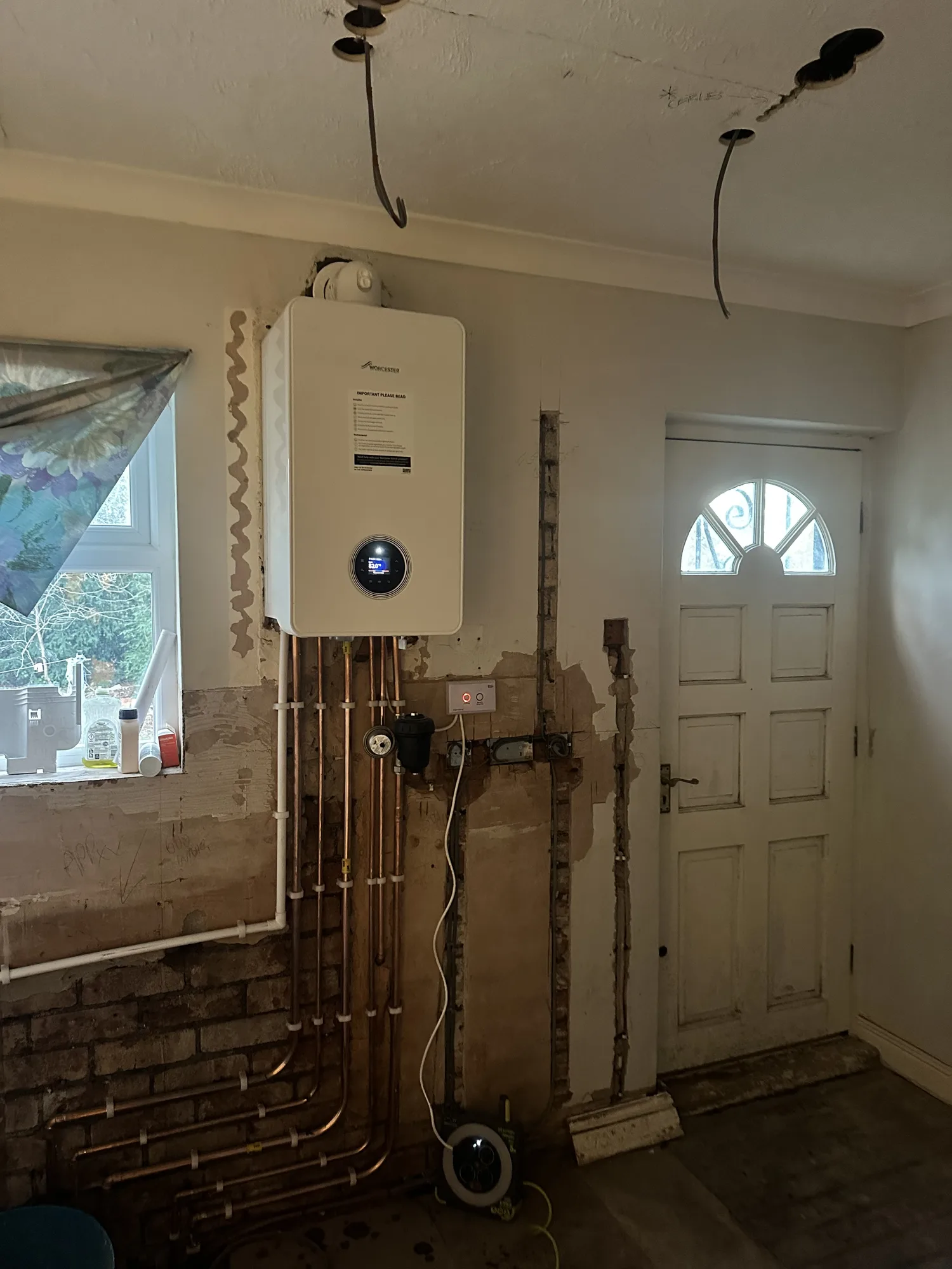 Wall-mounted gas boiler mid-installation with fresh copper pipework