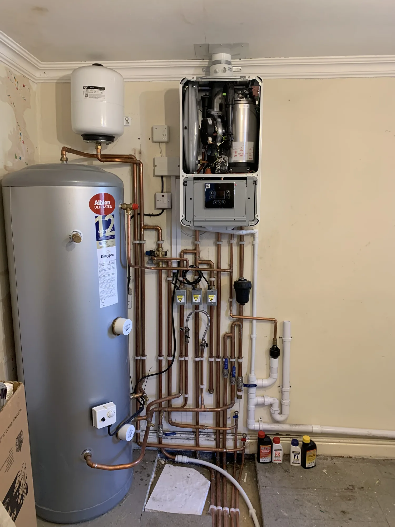 Gas combi boiler beside an unvented hot water cylinder and copper pipework