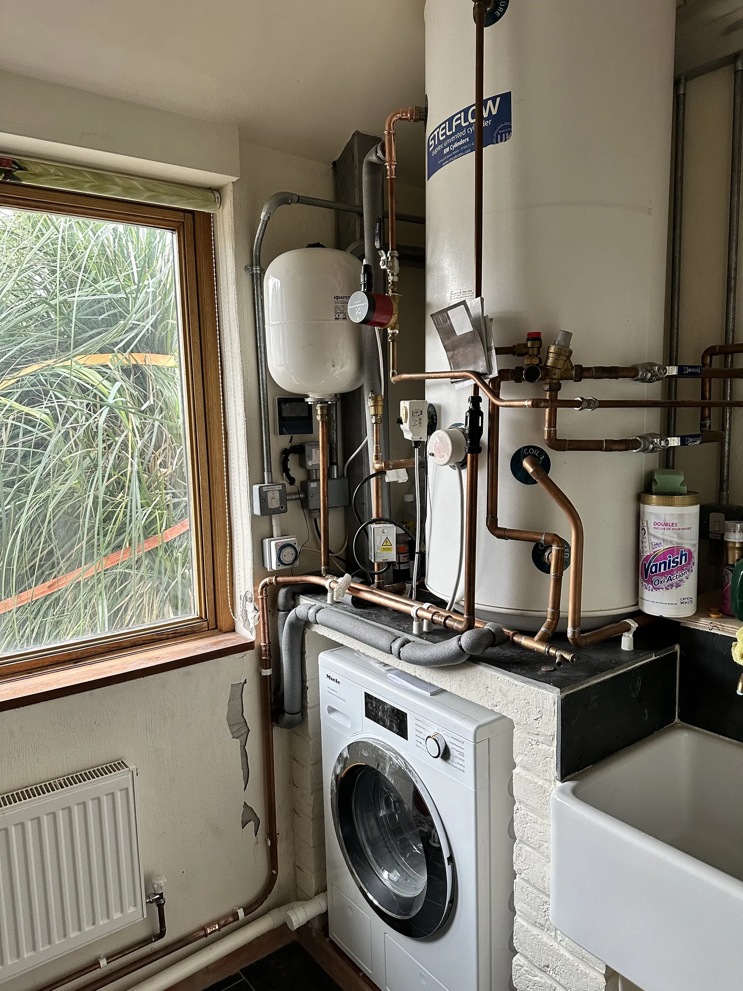 Vented hot water cylinder with header tank and copper pipework in a utility room