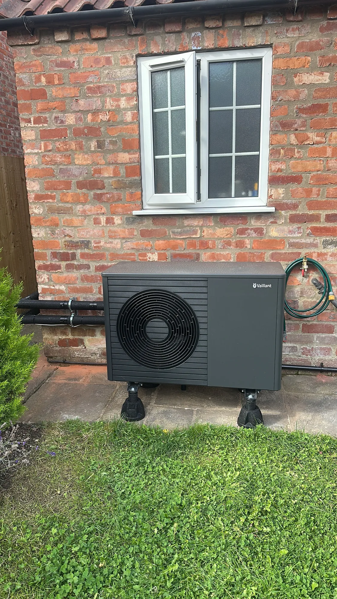 Air source heat pump installed on a rear patio beside a brick house